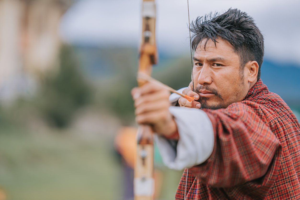 Bhutanese Man practicing archery aiming and shooting  in field